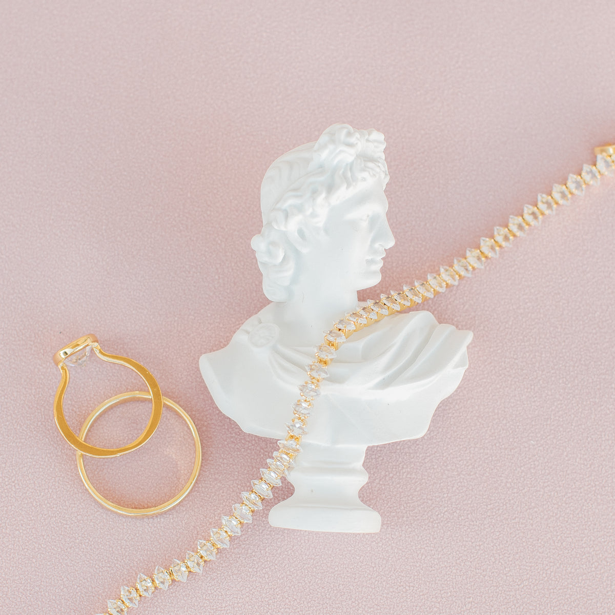 Mini white classical bust statue on blush fabric, styled with gold wedding bands and a crystal bracelet