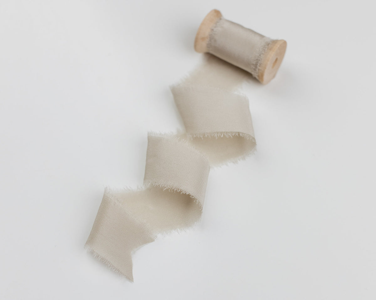 Fawn taupe silk ribbon draped from a wooden spool on white