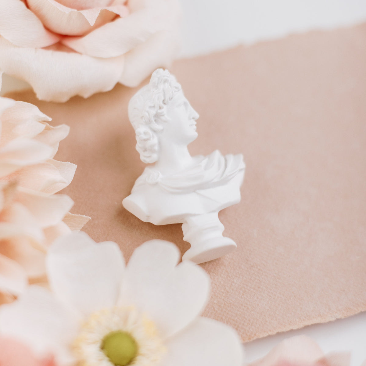 Mini white bust statue in side profile on blush paper beside cream flowers