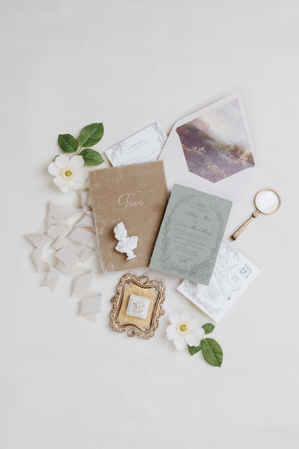 Invitation suite flat lay with envelopes, magnifier, ornate tray and a mini white bust statue as accent