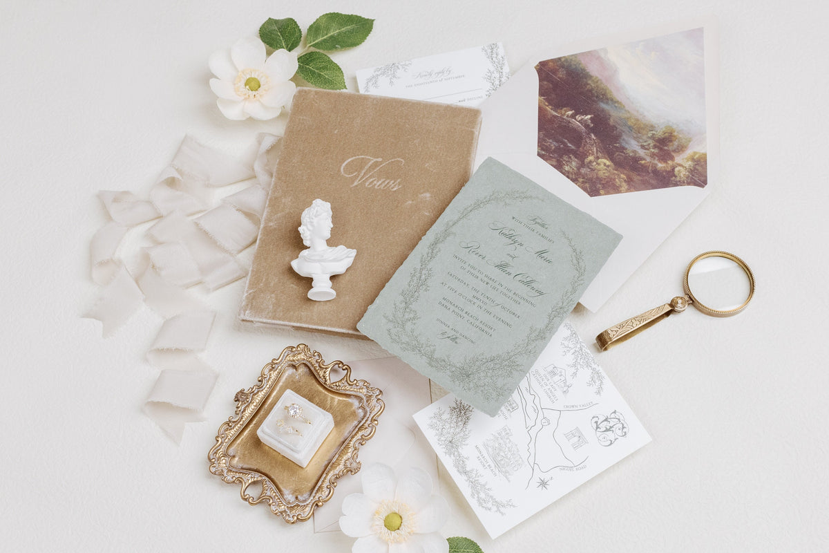 Wedding stationery flat lay with a mini white bust statue resting on a tan invitation card