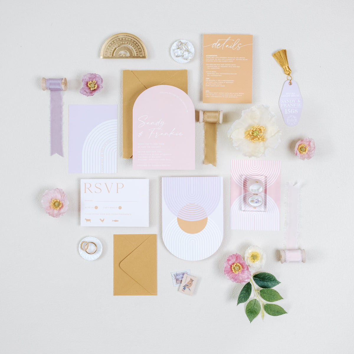 Pastel arched invitation suite flat lay with a mini white scalloped ring dish at lower left holding a ring
