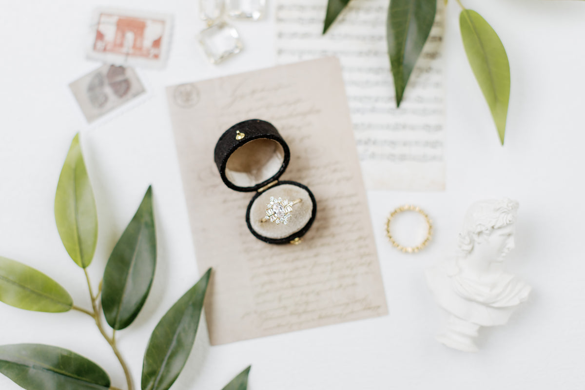 Mini white bust statue beside a black ring box with rings, on handwritten letter paper with green leaves