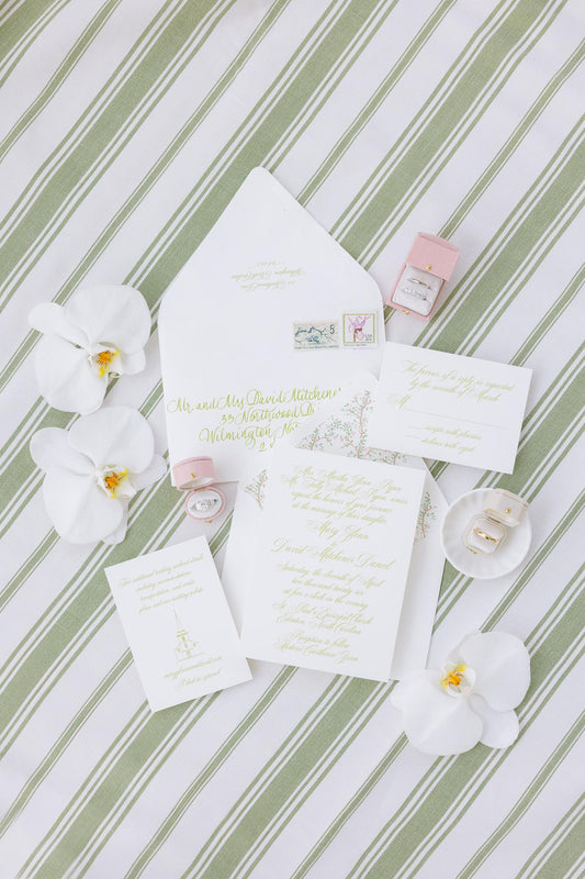 Invitation flat lay on green ticking stripe with white orchids, Georgian Square in Roseate, Georgian Oval in Roseate and Georgian Radiant in Dove ring boxes and a scalloped mini plate